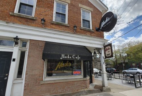 Exterior of Heck's Cafe featuring a brick facade, awning, and an "OPEN" sign in the window on a sunny day.