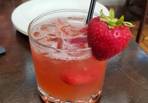 A refreshing strawberry drink with ice, garnished with a fresh strawberry, served in a clear glass on a wooden table.