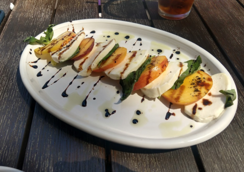A plate of sliced mozzarella and tomatoes, drizzled with balsamic glaze and garnished with basil leaves.