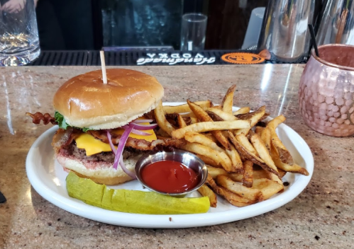 A juicy burger with cheese, bacon, and toppings, served with crispy fries, a pickle, and a side of ketchup.