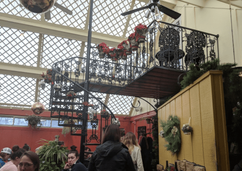 A cozy restaurant interior featuring a spiral staircase, festive decorations, and patrons enjoying their meals.