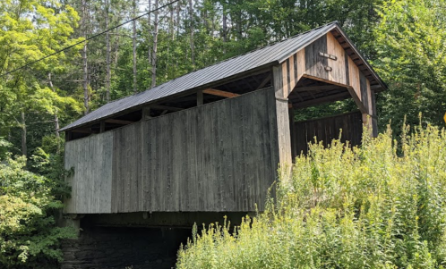 A rustic covered bridge with a wooden structure, surrounded by lush greenery and trees.