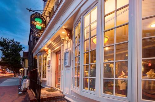 Exterior of Bolchard Restaurant at dusk, featuring large windows and a welcoming sign. Warm lights illuminate the entrance.