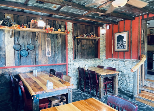 Cozy rustic restaurant interior with wooden tables, stone walls, and warm lighting, featuring autumn decorations.