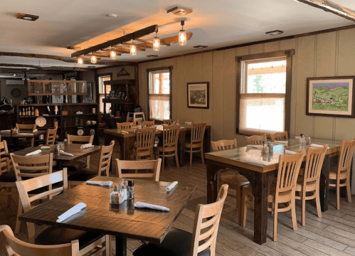 Cozy restaurant interior with wooden tables, chairs, and warm lighting, featuring artwork on the walls.