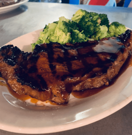 A grilled steak with a glossy glaze, served alongside steamed broccoli on a white plate.
