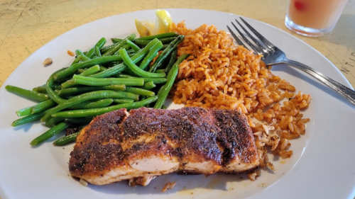 A plate with seasoned salmon, green beans, and rice, garnished with lemon wedges.