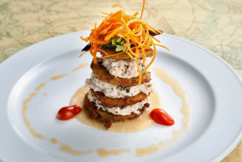 A stacked dish featuring crispy layers, shredded chicken, topped with carrot strips and drizzled with sauce.