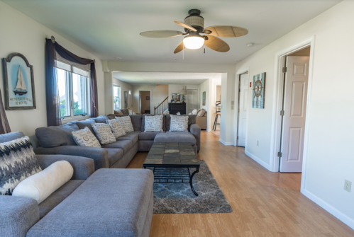 A spacious living room with a large gray sectional sofa, ceiling fan, and light wood flooring.