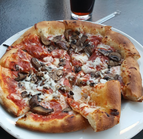 A slice of pizza topped with mushrooms and cheese on a white plate, with a glass of soda in the background.