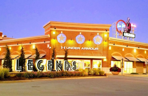 Exterior of a retail store featuring "Under Armour" signage and a large "Legends" display at dusk.