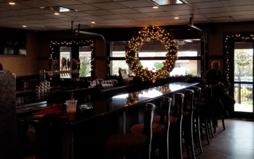 A dimly lit bar with a large festive wreath and holiday decorations, featuring a long counter and a few patrons.