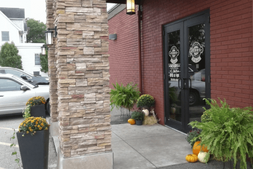 Entrance of a restaurant with stone pillars, potted plants, and decorative pumpkins on the ground.