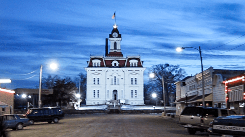 Historic courthouse at dusk, surrounded by streetlights and buildings, with a cloudy blue sky overhead.