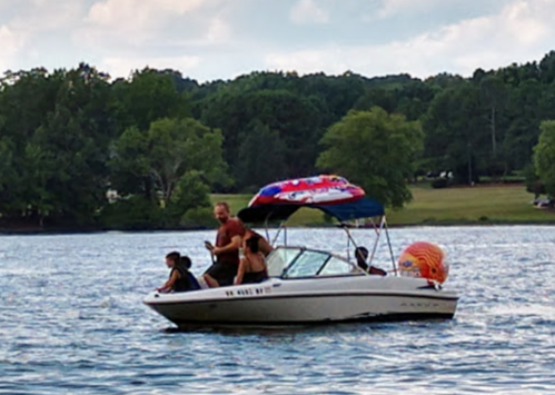 A group of four people on a boat enjoying a day on the water, surrounded by trees and a cloudy sky.
