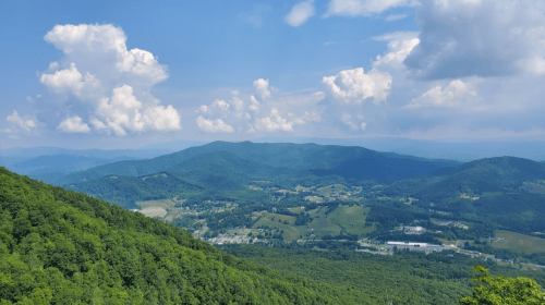 A panoramic view of lush green mountains under a blue sky with fluffy white clouds.
