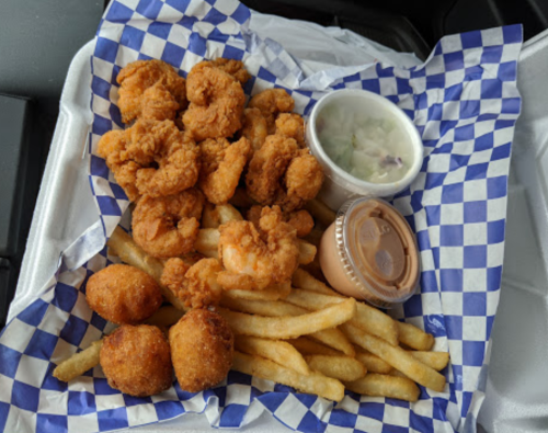 A tray of fried shrimp, French fries, hush puppies, and dipping sauces on a blue and white checkered paper.