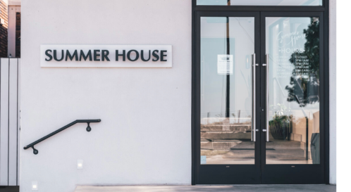 Exterior view of a building entrance with a sign reading "SUMMER HOUSE" and glass doors.
