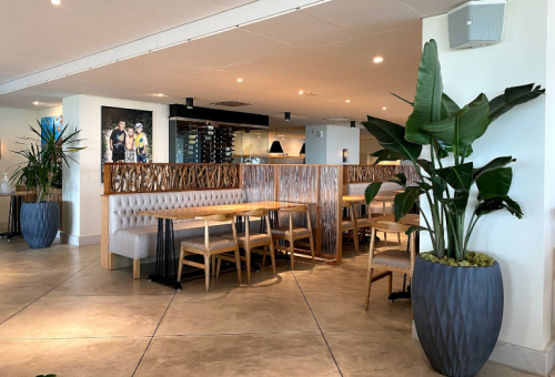 Modern restaurant interior featuring wooden seating, plants, and a stylish decor with a view of the kitchen area.