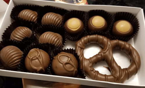 A box of assorted chocolates, including pretzels and various shaped truffles, arranged neatly in paper liners.