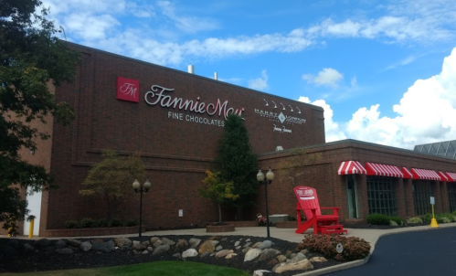 Exterior of Fannie May Fine Chocolates building with a red-striped awning and a large red chair in front.