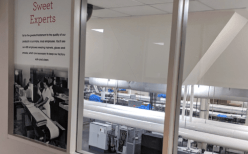 A view through a window into a factory, showcasing machinery and a sign about product quality and employee care.