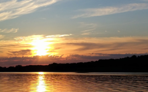 A serene sunset over a calm lake, with vibrant orange and yellow hues reflecting on the water's surface.