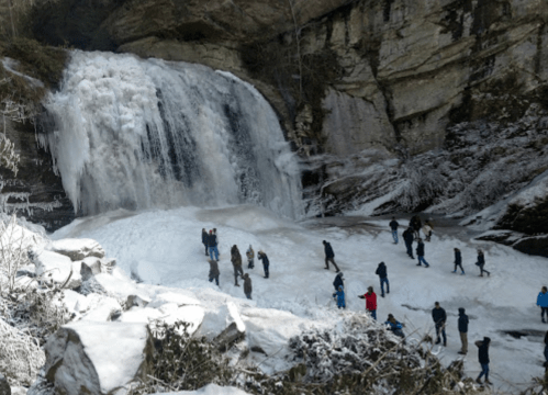 People exploring a frozen waterfall surrounded by snow-covered rocks and trees.