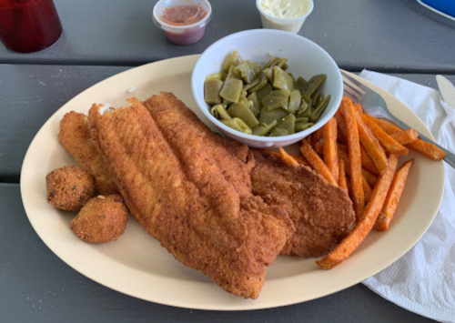 A plate of fried fish fillets, sweet potato fries, green beans, and hushpuppies, with dipping sauces on the side.