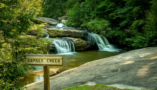 A serene view of Ramsey Creek with cascading waterfalls surrounded by lush greenery and smooth rock formations.