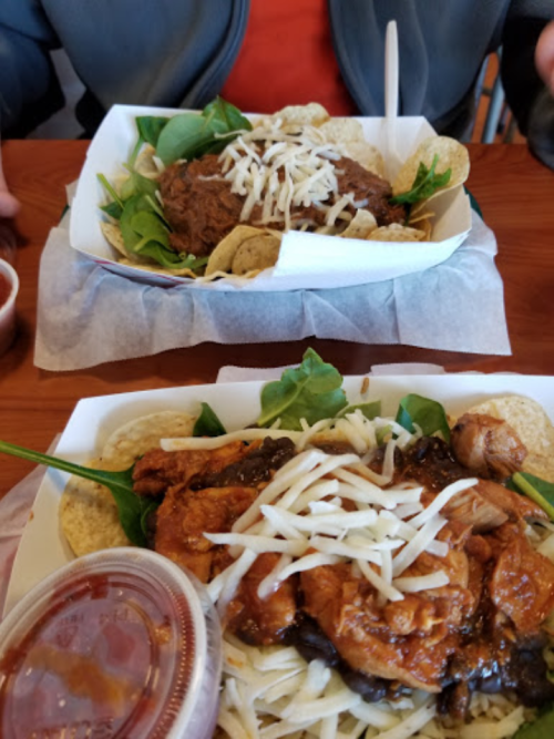 Two plates of food featuring chicken, greens, cheese, and tortilla chips, with a side of sauce.