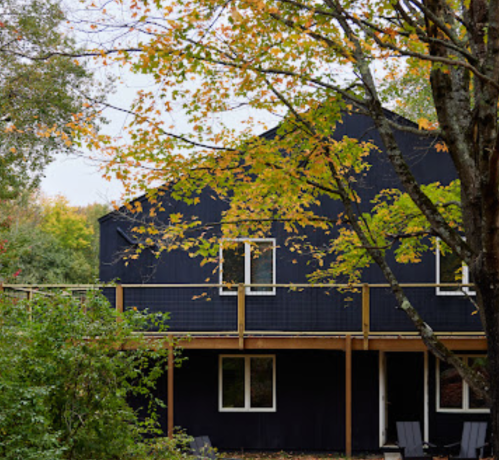 A modern black house surrounded by colorful autumn trees and greenery.