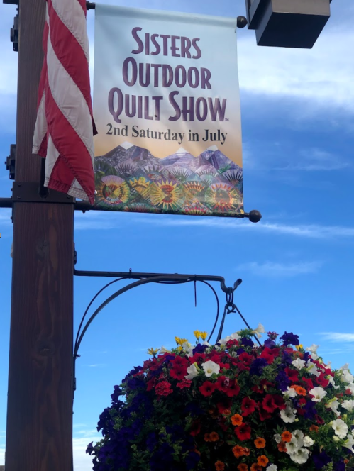 A banner for the Sisters Outdoor Quilt Show, featuring colorful flowers and mountains under a blue sky.
