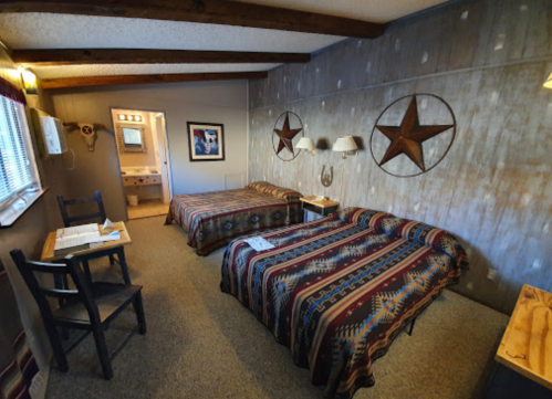 Cozy hotel room with two beds, rustic decor, and a small desk, featuring star wall art and a bathroom in the background.