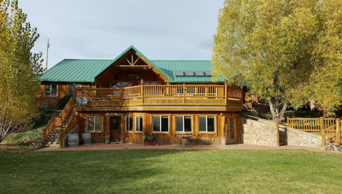 A large wooden house with a green metal roof, surrounded by trees and a grassy area.