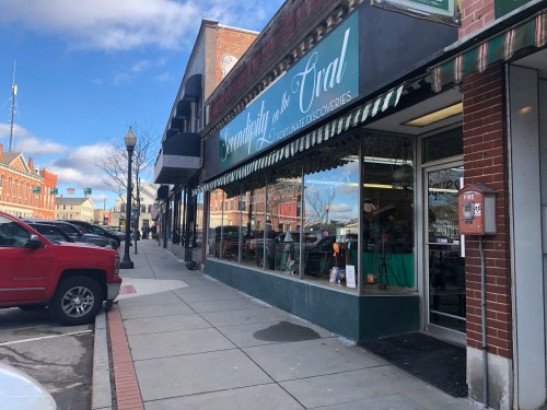 A storefront with a green sign reading "Goodnight & Co." on a sunny day, with parked cars and a brick building nearby.