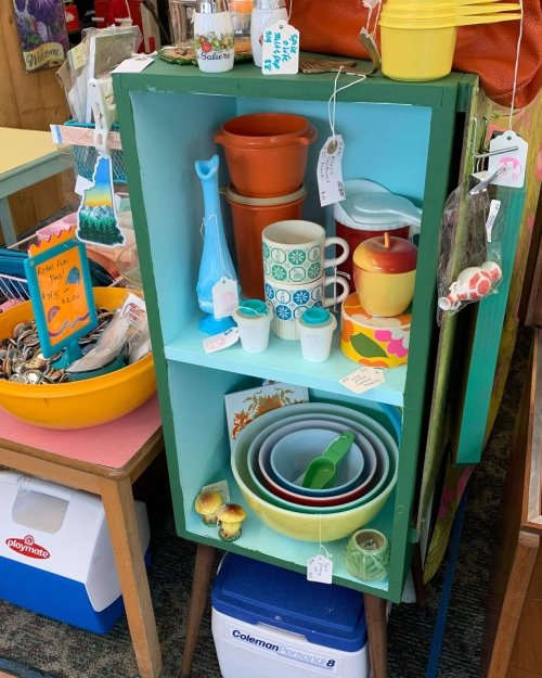 A colorful display of vintage kitchenware and decor items on shelves, including bowls, cups, and decorative pieces.
