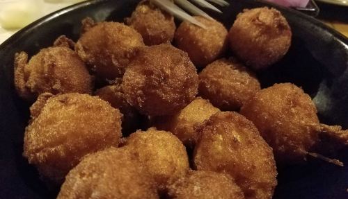 A black bowl filled with golden-brown, crispy fried balls, likely seafood or vegetable fritters.