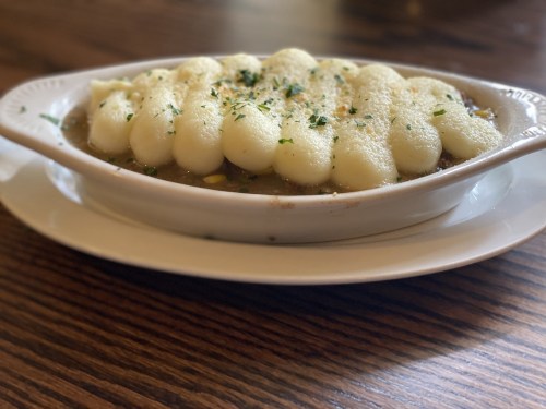 A dish of creamy mashed potatoes topped with herbs, served in a white oval dish on a wooden table.