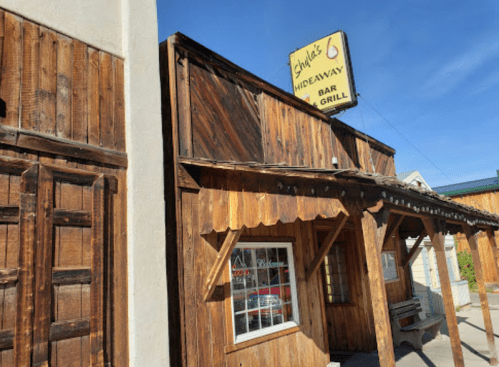 A rustic wooden building with a sign reading "Judy's Hideaway Bar & Grill" under a clear blue sky.