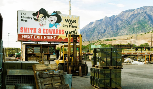 Billboard advertising "Smith & Edwards" with mountains in the background, surrounded by storage containers and a forklift.