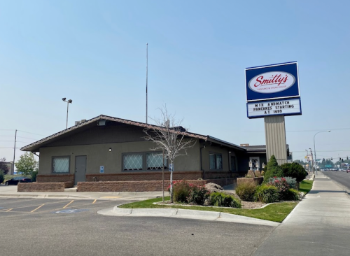 Exterior of Smitty's restaurant with a sign, featuring a parking lot and surrounding landscaping on a sunny day.