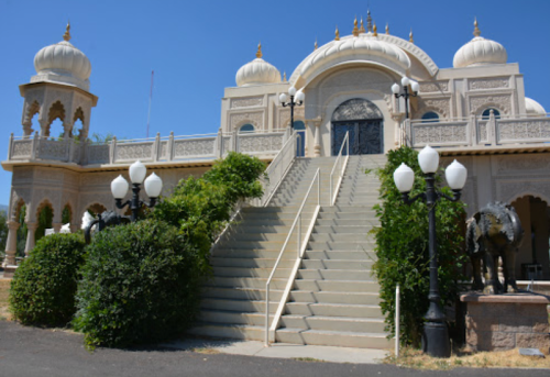 A grand building with ornate architecture, featuring a staircase, decorative lamps, and lush greenery.