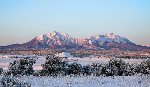 Snow-covered mountains rise against a clear sky, surrounded by a winter landscape of white and green vegetation.