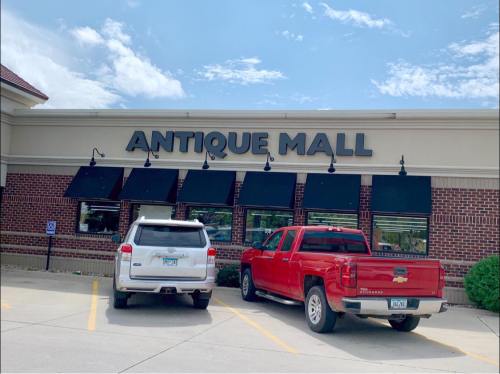 Exterior of an Antique Mall with a white SUV and a red pickup truck parked in front. Clear blue sky above.