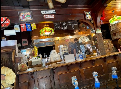 Interior of a cozy restaurant with a wooden counter, menu board, and colorful stained glass lamps.