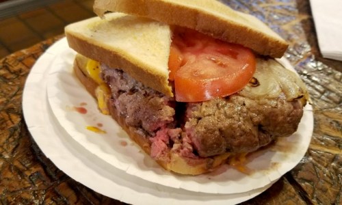 A sandwich with a thick beef patty, melted cheese, tomato slices, and onions, served on two slices of bread.
