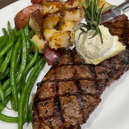A plate featuring a grilled steak, green beans, and roasted red potatoes topped with a dollop of butter.