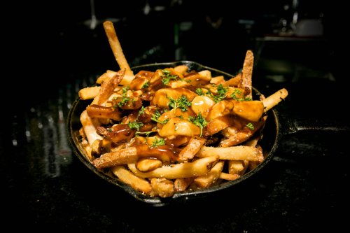 A skillet filled with crispy fries topped with gravy and chunks of meat, garnished with fresh herbs.