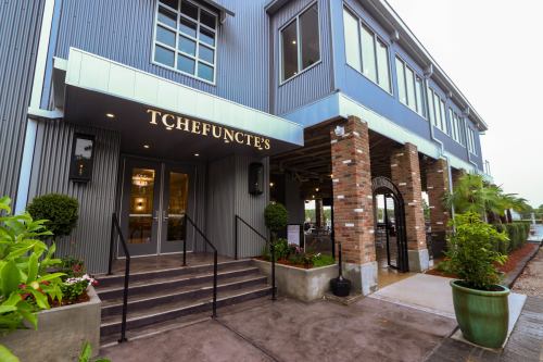 Exterior of Tchefuncte's restaurant featuring a modern design with brick and metal elements, surrounded by greenery.